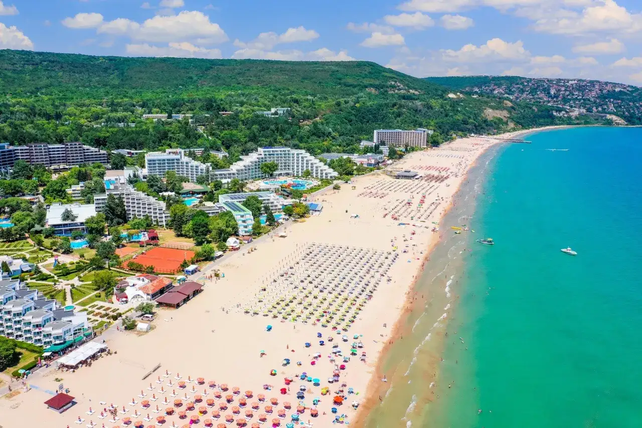 Słoneczna plaża w Bułgarii, pełna turystów i leżaków. W tle hotele i zielone wzgórza. Czy w Bułgarii jest bezpiecznie? Wygląda na to, że tak, skoro tylu ludzi wypoczywa.