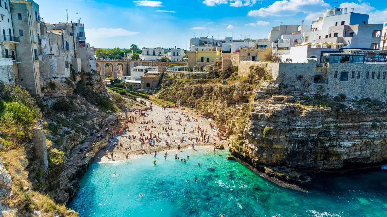 Malownicze bari plaże z białymi domami na klifach i turkusową wodą. Ludzie odpoczywają na kamienistej plaży i kąpią się w morzu.