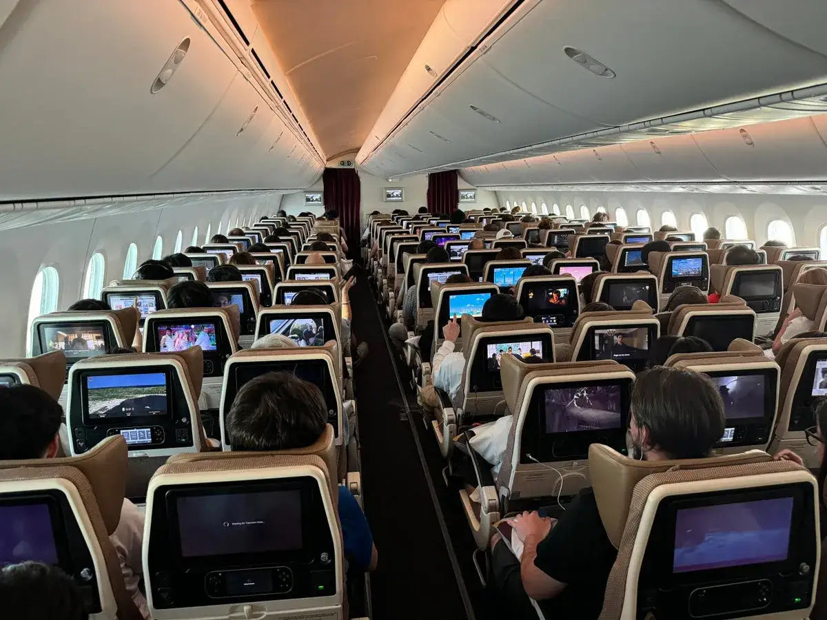 Wnętrze samolotu Etihad Airways, pełne pasażerów oglądających filmy na ekranach. Dobre etihad airways opinie potwierdzają komfort podróży.