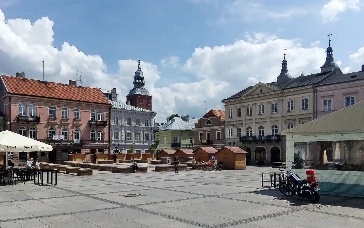 Rynek w Piotrkowie Trybunalskim z kamienicami, wieżą i kawiarnianymi ogródkami. Atrakcje Piotrkowa Trybunalskiego zachęcają do spacerów.