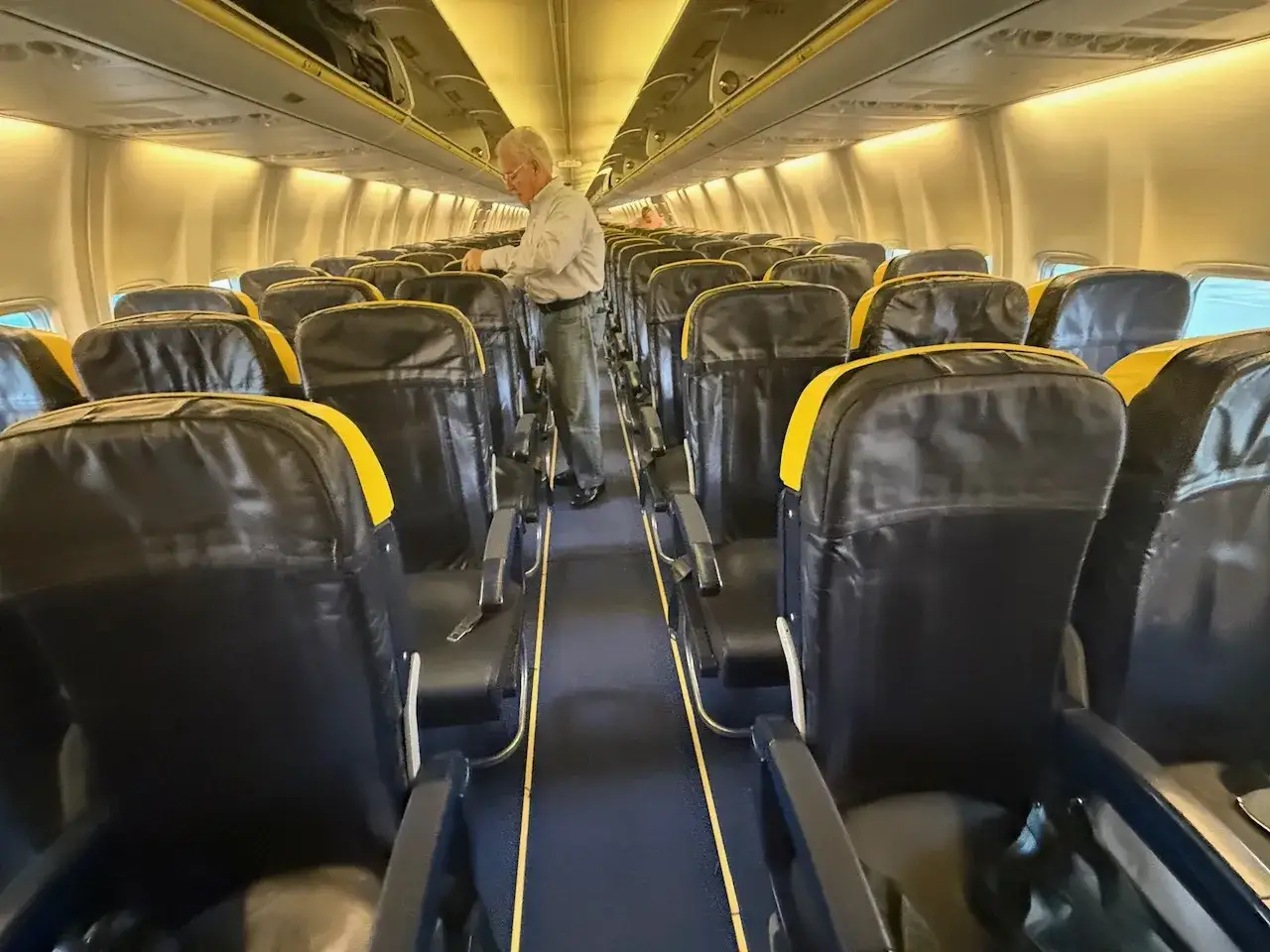 Pasażerowie zastanawiają się, ile jest miejsc w samolocie Ryanair. Wnętrze samolotu z rzędami czarnych siedzeń i żółtymi zagłówkami.