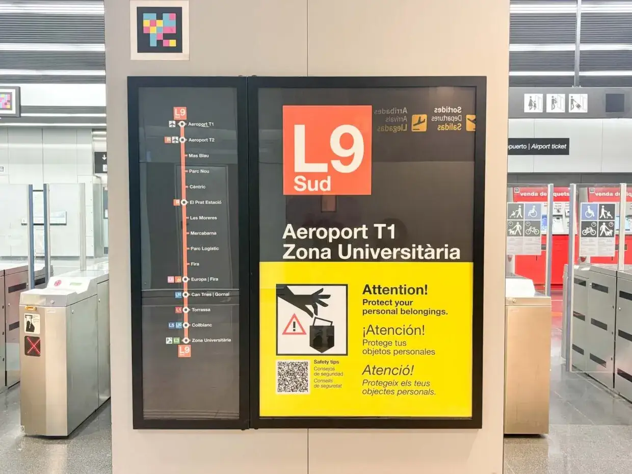 Tablica informacyjna na barcelona lotnisko pokazuje trasę metra L9 Sud do Aeroportu T1 i innych stacji. Ostrzeżenie przypomina o pilnowaniu rzeczy.